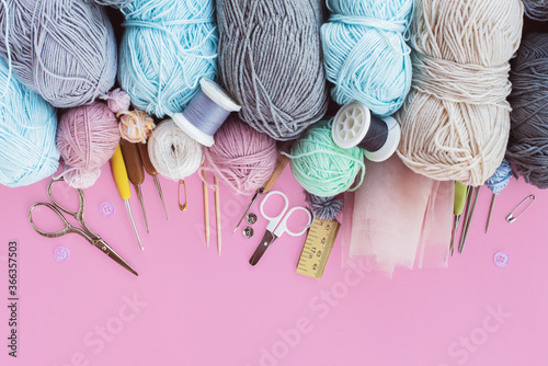 Women's hobby. Multicolored skeins, needles, hooks on the pink background. Conept of sewing, crochet and knitting. 