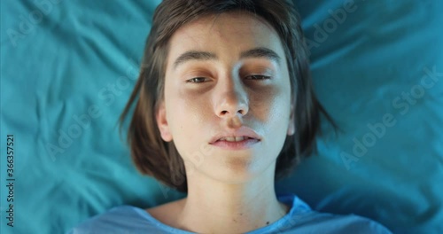 Top view of millennial unconscious girl lying on medical transportation cart. Close up of young ill woman riding in ambulance to hospital. Concept of illness and healthcare