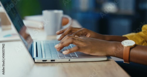 Close up shot of African American female hands typing on laptop while sitting at office desk indoors. Woman fingers tapping and texting on computer keyboard while working in cabinet. Work concept photo
