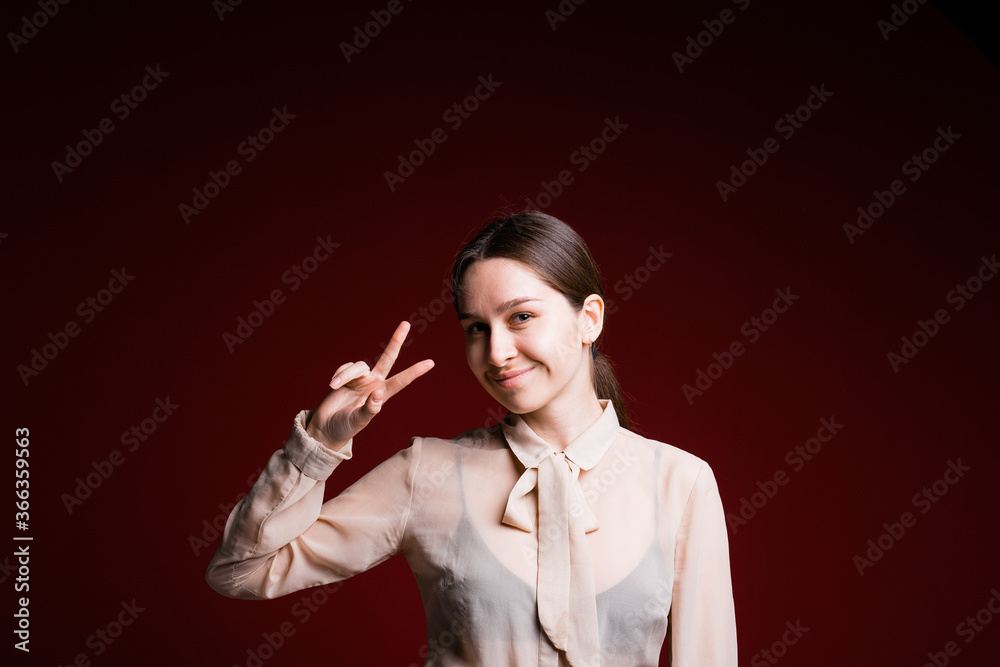 Portrait of a business girl who smiles cheerfully and shows a victory sign with her fingers on a red background Portrait of a business girl who smiles cheerfully and shows a victory sign with her fingers on a red background