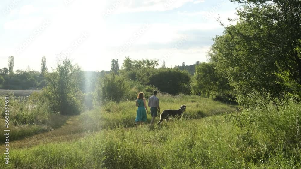 Young Couple walk in the park with their irish wolfhound dog at sunrise/sunset. Animal care concept Young Couple walk in the park with their irish wolfhound dog at sunrise/sunset. Animal care concept