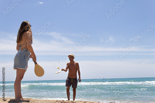Young beautiful couple playing paddle ball on the beach in summer (tennis).Happy Holidays  concept lifestyle.