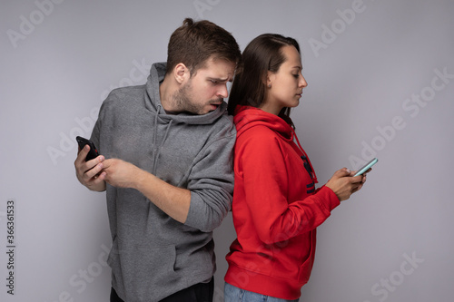 Young couple using smartphones at home. Jealous boyfriend spying his girlfriend's phone.