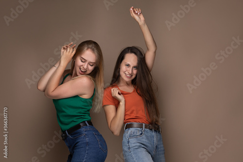 Full-length shot of blithesome curly girl in denim pants. Stunning blonde female model jumping while her friend dancing.