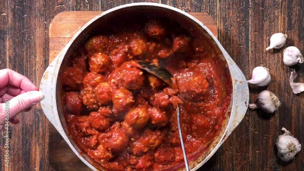 overhead view of ladle stirring large pot of homemade meatballs and spaghetti sauce overhead view of ladle stirring large pot of homemade meatballs and spaghetti sauce