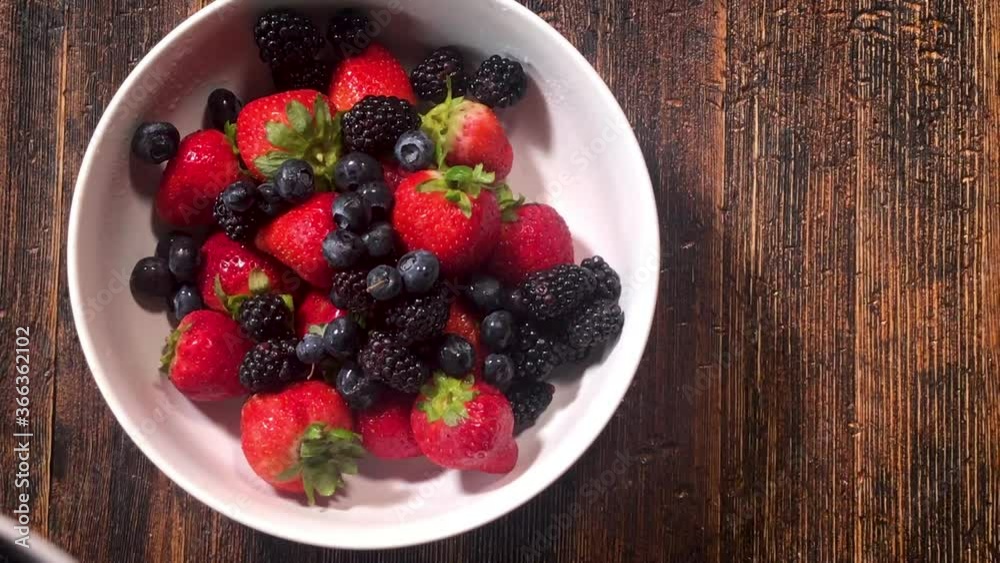 adding fresh berry mix of strawberries, blueberries, and blackberries to bowl on table adding fresh berry mix of strawberries, blueberries, and blackberries to bowl on table