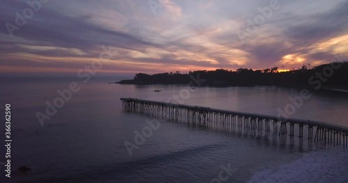 Beautiful Aerial Footage of Long Pier in Bay with dark Island Forest silhouette and Sunset with Pink Sky