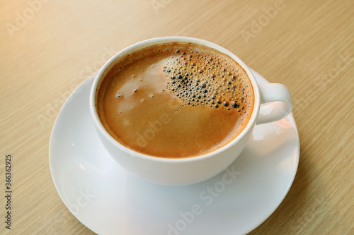 Cup of hot coffee with frothy surface isolated on wooden table
