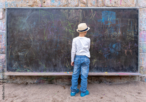 cute little boy writing something with chalk on blackboard