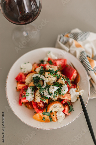 Tomato crostini salad with mozzarella cheese. Refreshing healthy dinner. Glass of red wine. Nourishing salad lunch. Panzanella heirloom tomato summer seasonal Italian salad. Colorful plate.