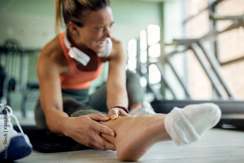 Close-up of female athlete feeling pain in her ankle during sports training at health club. - obrazy, fototapety, plakaty 