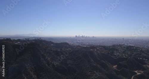 Aerial of the Hills in Hollywood with Los Angeles Observatory shown on Mountain Top, Downtown Skyscrapers shown in Horizon and Blue Sunny Sky