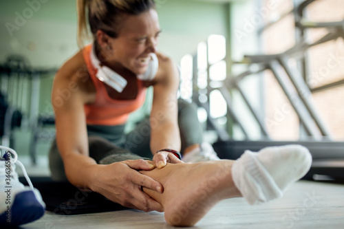 Close-up of female athlete feeling pain in her ankle during sports training at health club.