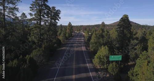 Aerial of small Road in Countryside with Forest and Blue sky showing sign Crossing Between Albuquerque and Flagstaff before entering Highway