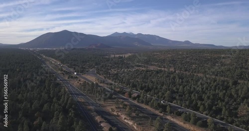Aerial footage of Highway going through Forest with Big mountain chain in Horizon and Blue Sky at Arizona New Mexico Border