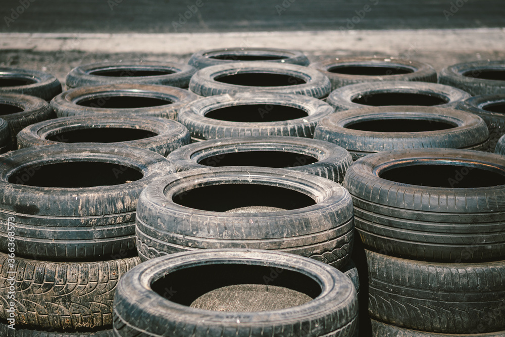 Many old used car tires stacked on top of each other on Automobile sports complex. Industrial landfill for the processing of waste tires and rubber tyres. Old rubber wheels. Tires on the autodrome Many old used car tires stacked on top of each other on Automobile sports complex. Industrial landfill for the processing of waste tires and rubber tyres. Old rubber wheels. Tires on the autodrome