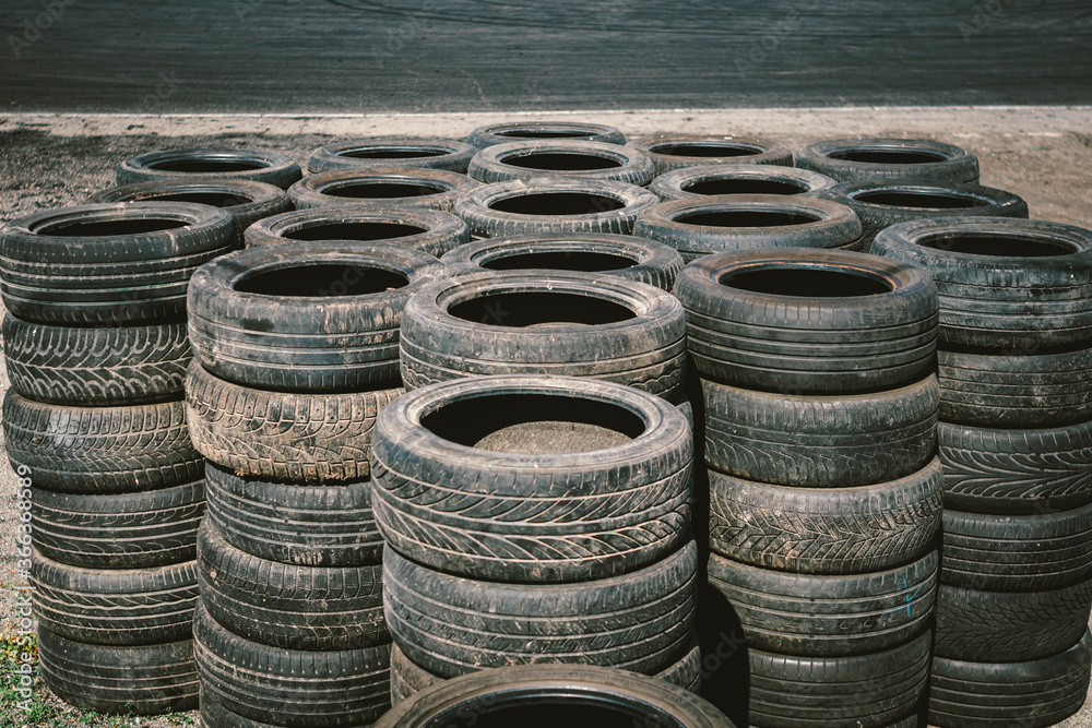 Many old used car tires stacked on top of each other on Automobile sports complex. Industrial landfill for the processing of waste tires and rubber tyres. Old rubber wheels. Tires on the autodrome Many old used car tires stacked on top of each other on Automobile sports complex. Industrial landfill for the processing of waste tires and rubber tyres. Old rubber wheels. Tires on the autodrome