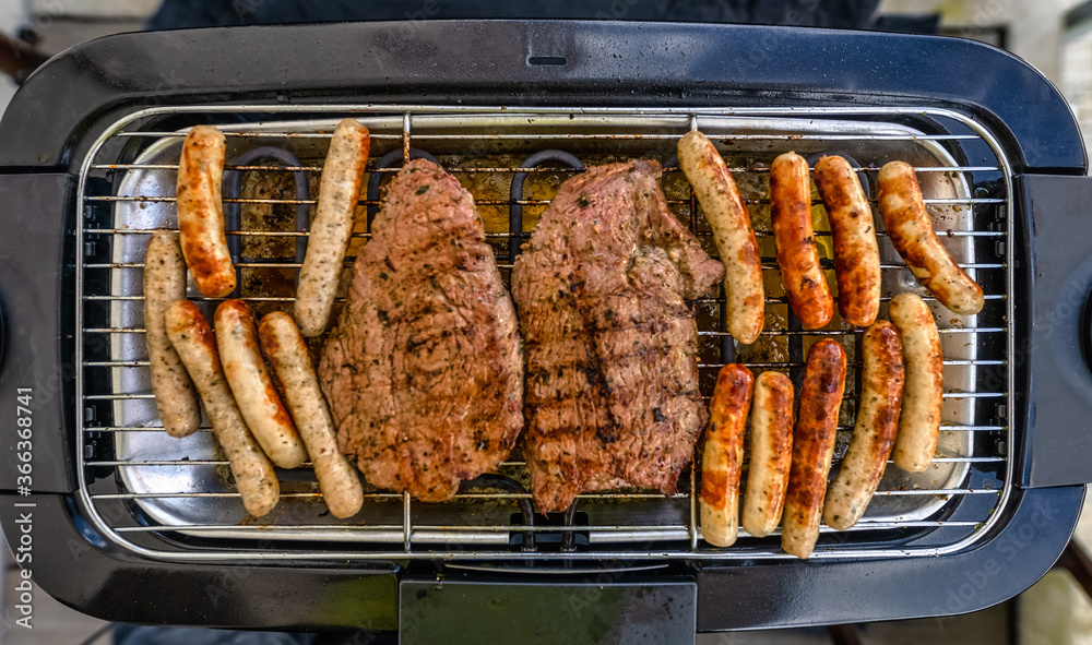 Top view at a bbq grill with meat of beef and little sausages called in germen Nuernberger, ready to eat in tasty condition. Top view at a bbq grill with meat of beef and little sausages called in germen Nuernberger, ready to eat in tasty condition.