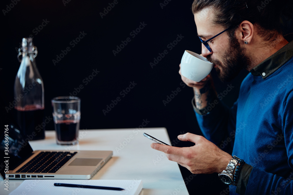 Side view of serious hipster sitting in his office and using smart phone. Side view of serious hipster sitting in his office and using smart phone.