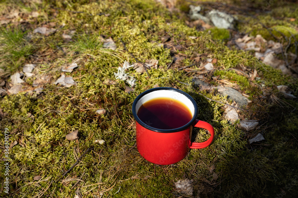 Obraz premium Metal vintage red mug on moss in forest. Black tea in red cup.