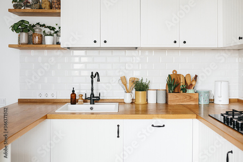 View on white kitchen in scandinavian style, kitchen details, plants on wooden table