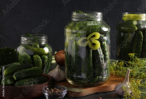Marinated cucumbers with garlic, pepper and dill in a glass jars on dark background, Closeup