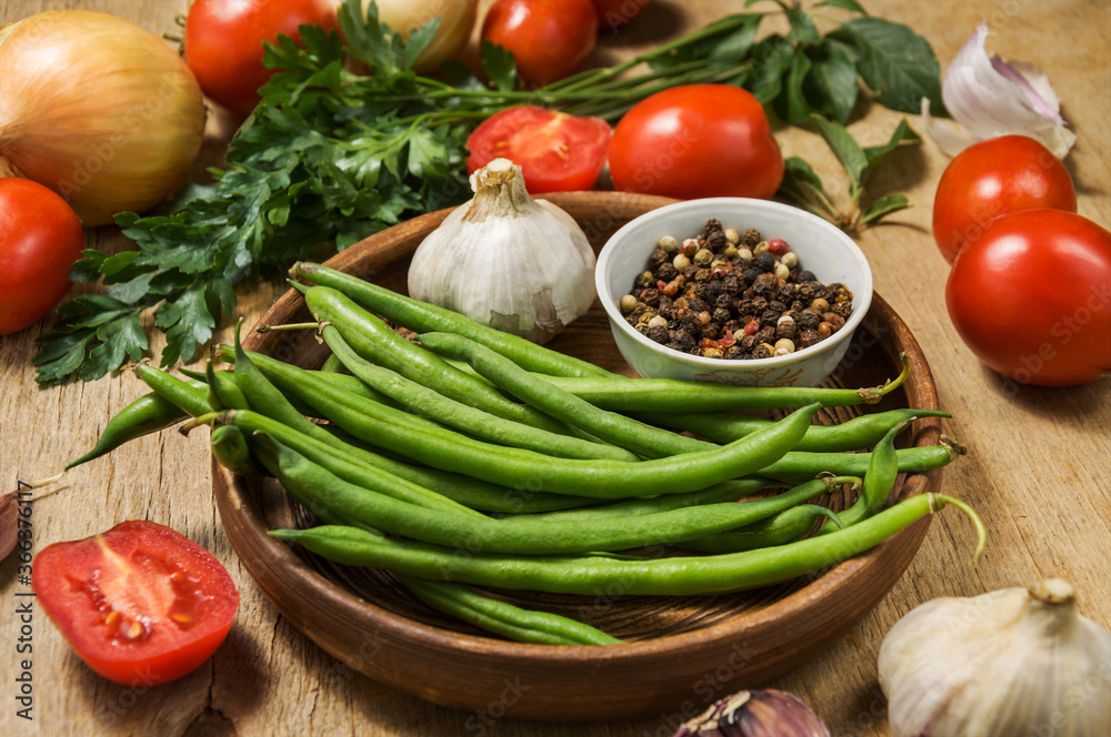 Fresh ripening vegetables on a wooden table. Zucchini, asparagus beans, tomatoes and garlic in a clay plate while preparing a vegetarian meal on the kitchen table.