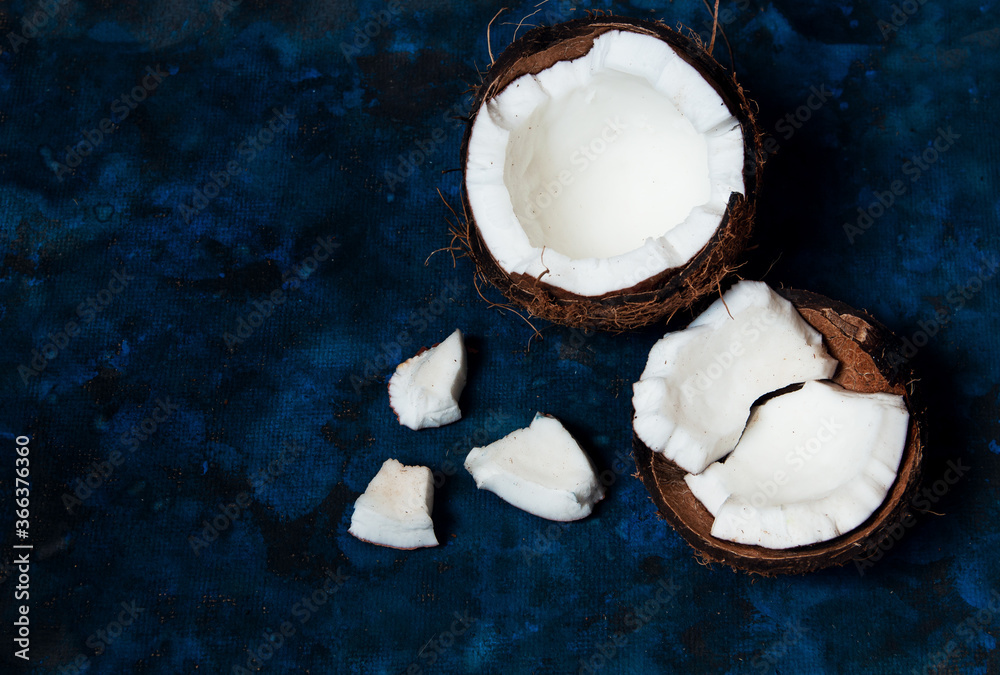 Open coconut lies on a dark blue background next to broken pieces lying randomly Open coconut lies on a dark blue background next to broken pieces lying randomly