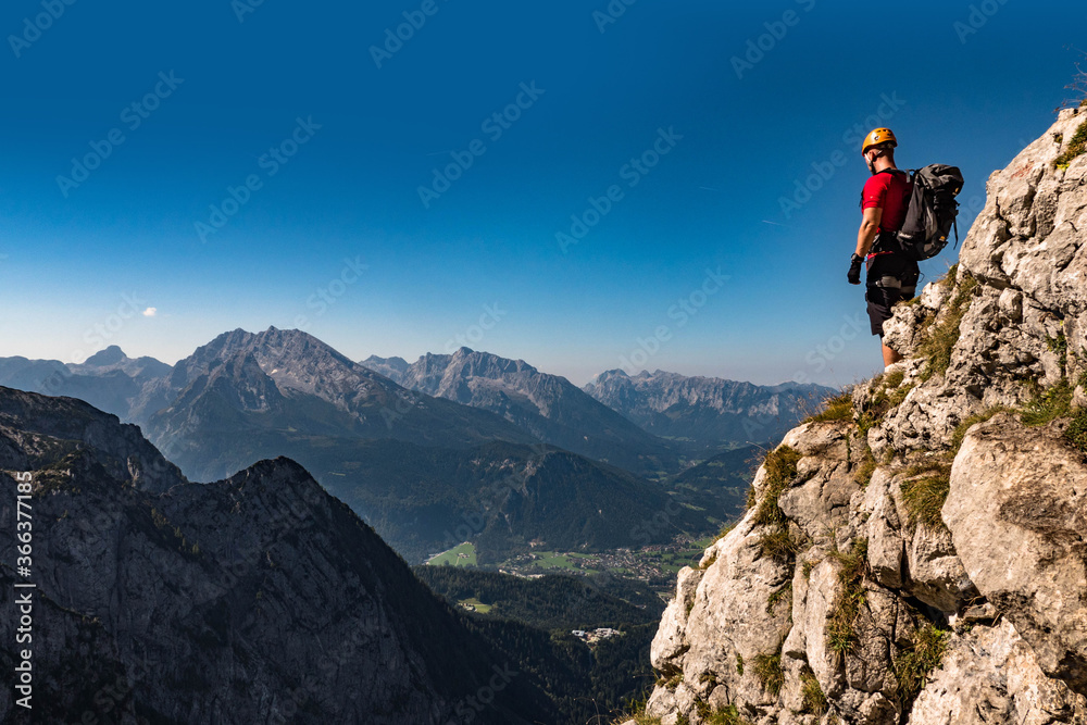 Male climber on the top of the mountain looking at the landscape, with helmet