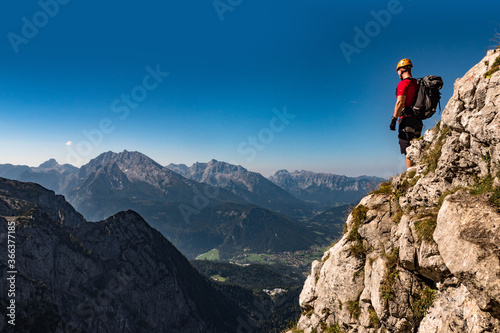 Male climber on the top of the mountain looking at the landscape, with helmet