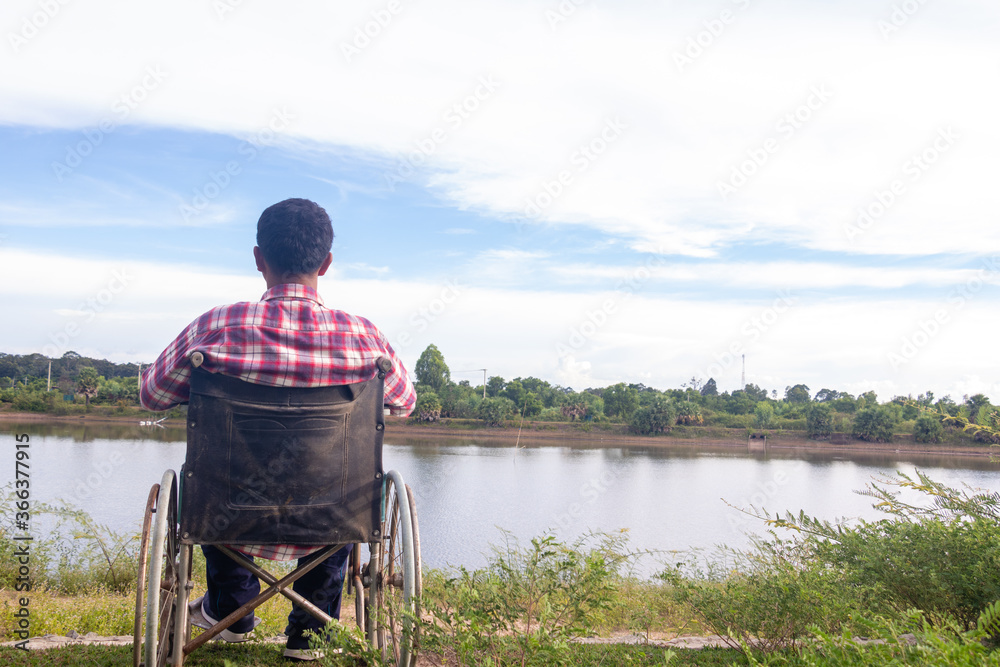 Obraz premium Young disabled man with river background.He is sitting on wheelchair and looking into river.