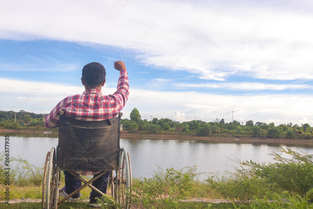 Obraz premium Young disabled man with river background.He is sitting on wheelchair and looking into river.