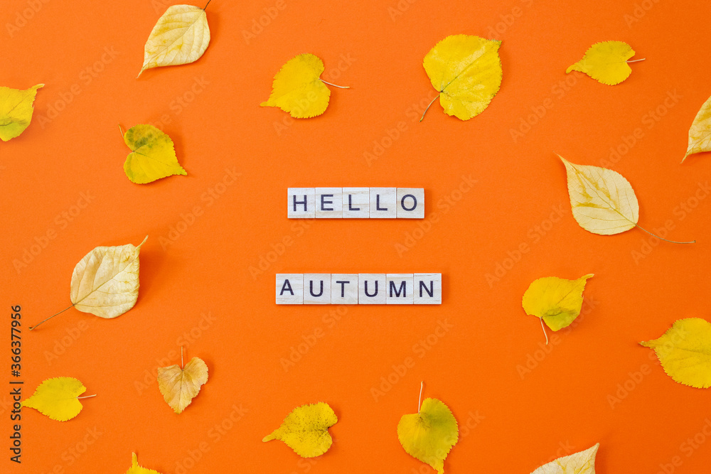 Words Hello Autumn. Wooden blocks with letters on orange background decorated with yellow leaves. Flat lay, top view.