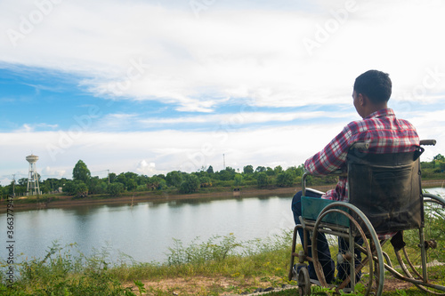Young disabled man with river background.He is sitting on wheelchair and looking into river.