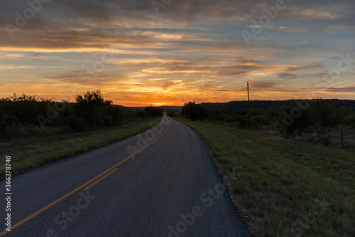 Rural country road leading to a beautiful orange sky at sunset