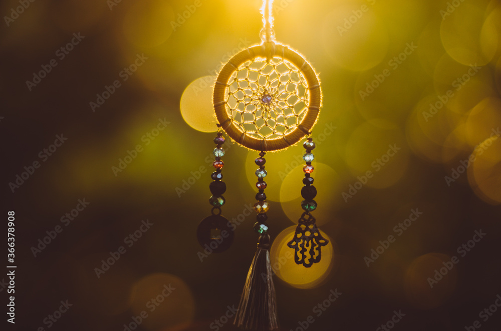 Close up of spiritual dreamcatcher necklace with sacred geometry circle with bokeh background backlit by sunset golden light Close up of spiritual dreamcatcher necklace with sacred geometry circle with bokeh background backlit by sunset golden light