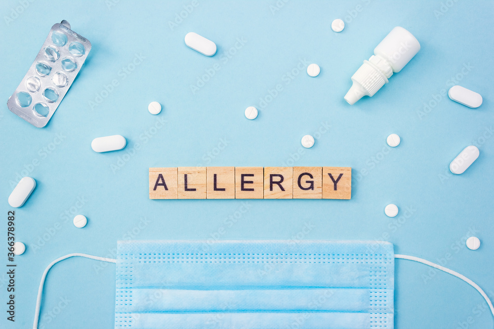 Word Allergy. Wooden blocks with letters on blue background surrounded by medical mask, pills and nasal drops. Top view, flat lay