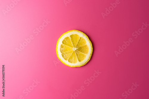 A single slice of lemon isolated on a pink background, illuminated by a soft light. photo