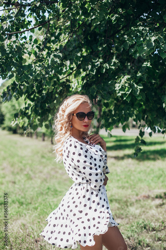 Beautiful fashion blonde hair girl in sexy polka dot dress walking at the park