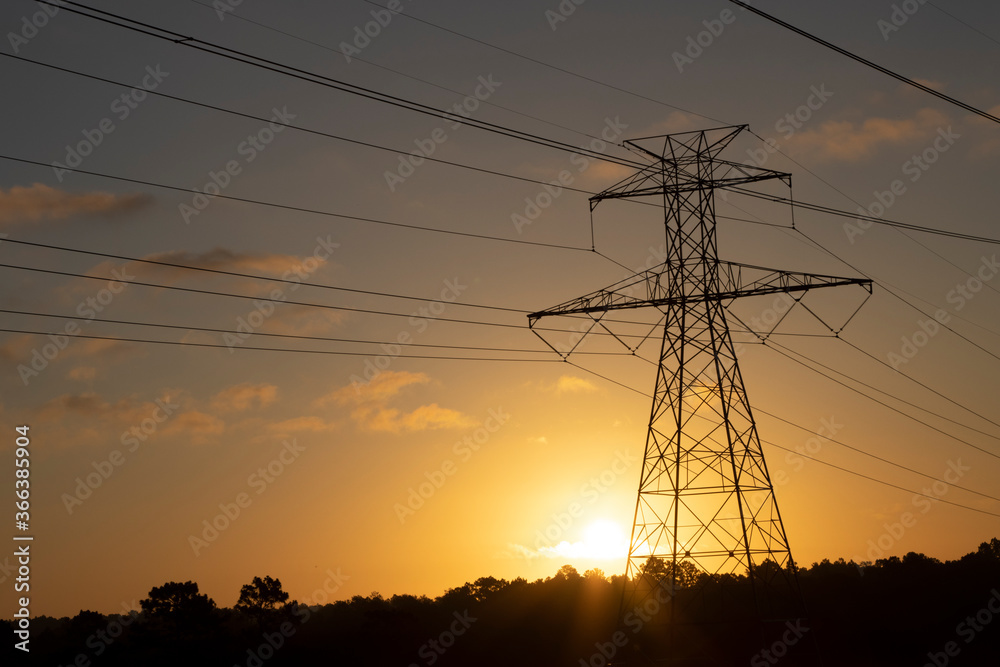 Fototapeta premium The sun rising behind a towering electricity pylon