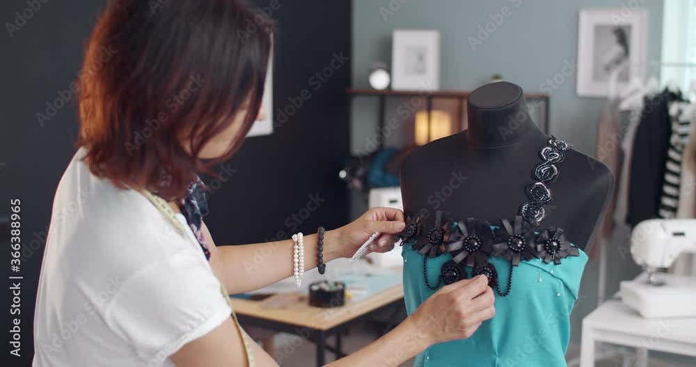 Attractive woman with dark hair creating new trendy dress at own atelier. Female designer using mannequin and sewing tools at work.