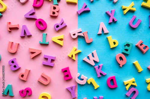 A set of letters for studying the alphabet. Multicolored wooden letters on a blue and pink background. Close-up, top view, flat lay.