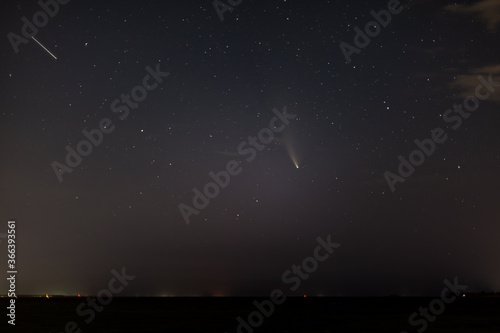 Comet NEOWISE, a satellite in the dark starry sky with clouds above the horizon at night. Horizontal orientation.  © Sander Studio