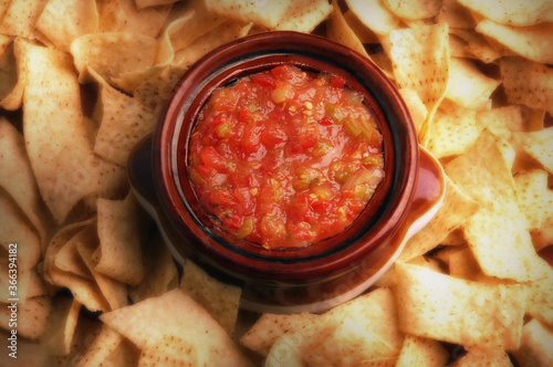 Flat lay still life image of a bowl filled with salsa surrounded by corn chips with warm side light.