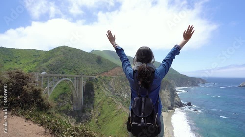 back view of young woman with hands raised outdoors in summer on top of mountains on a sunny day. concept of success and freedom and active lifestyle. carefree girl backpacker relax visit big sur