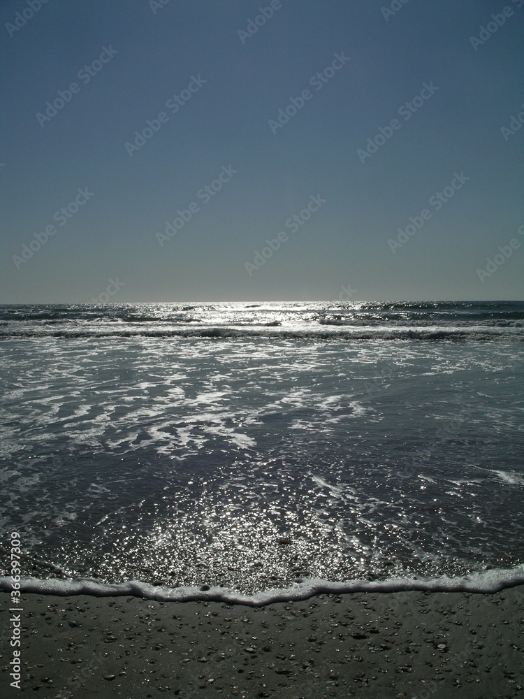 Sunlight Hitting Ocean Waves on Sandy Beach with Clear Cloudless Sky