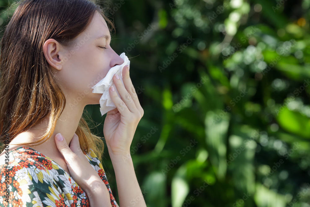 Seasonal allergies. Young girl blowing nose and sneezing in tissue in the park. Seasonal allergies. Young girl blowing nose and sneezing in tissue in the park.