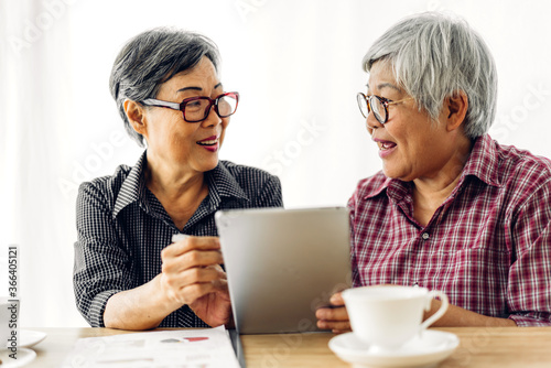 Portrait of two friend happy senior adult elderly asia women smiling and working with digital tablet computer at home.Retirement concept