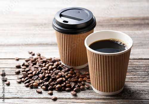 A paper cup of coffee and coffee beans on an old wooden background photo