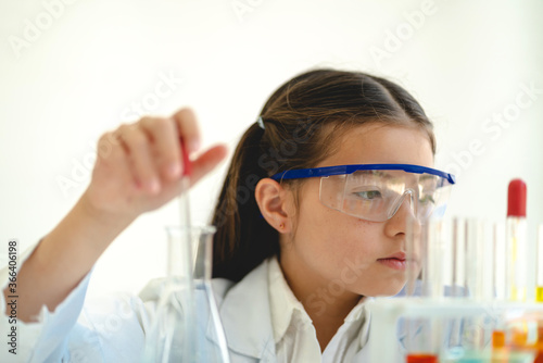 Cute little girl student child learning research and doing a chemical experiment while making analyzing and mixing liquid in glass at science class on the table.Education and science concept